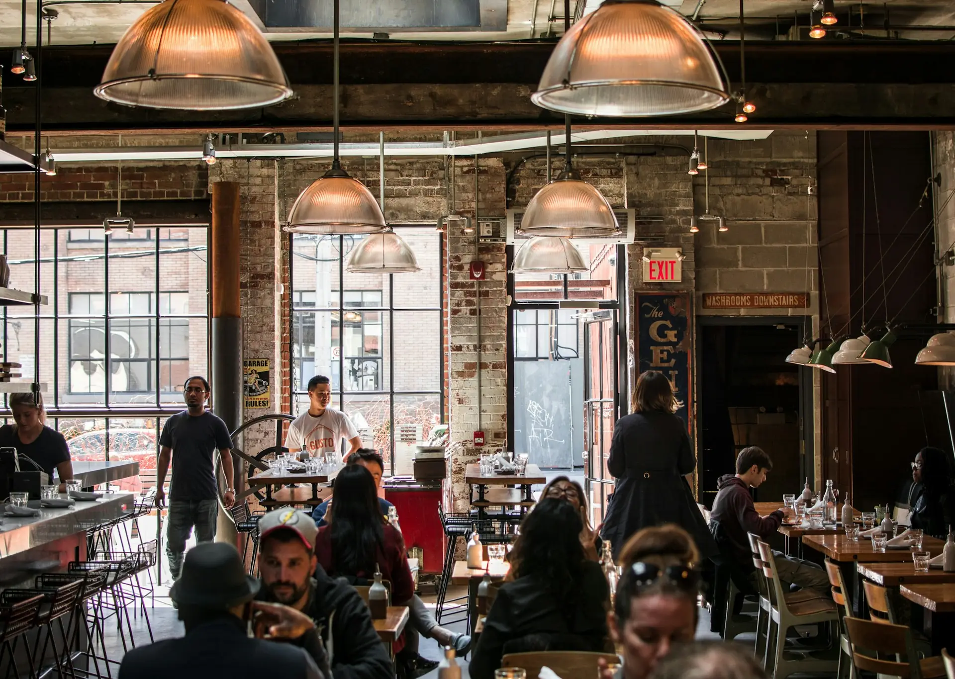 A busy, warmly lit café dining room with hanging pendant lamps