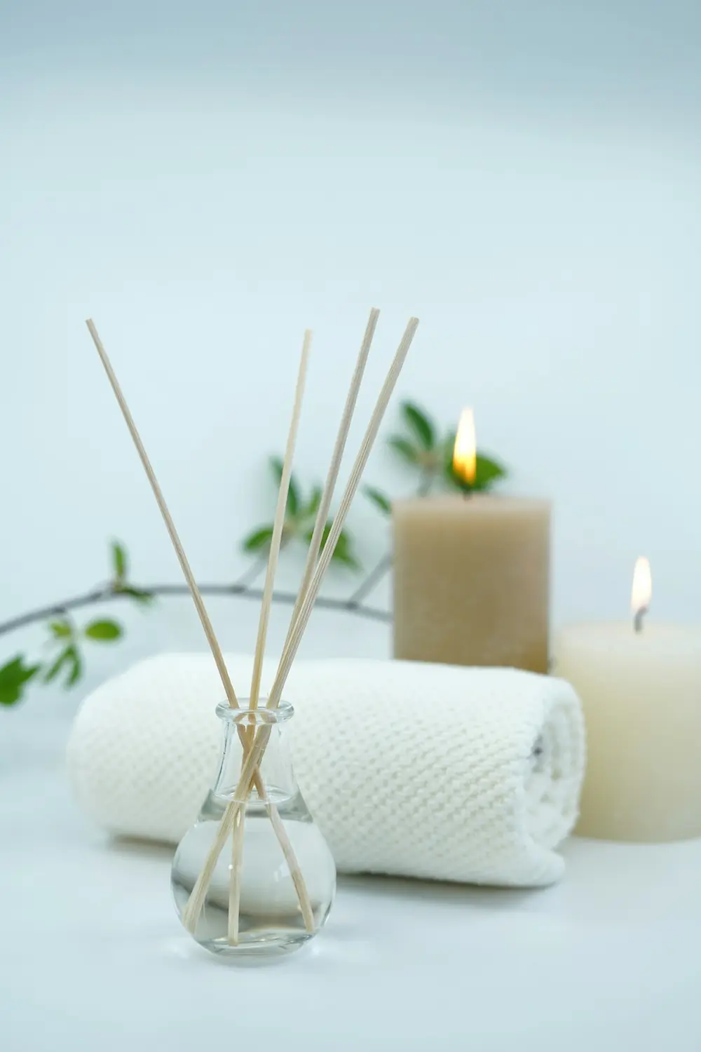 A reed diffuser, candles and a folded towel on a tray